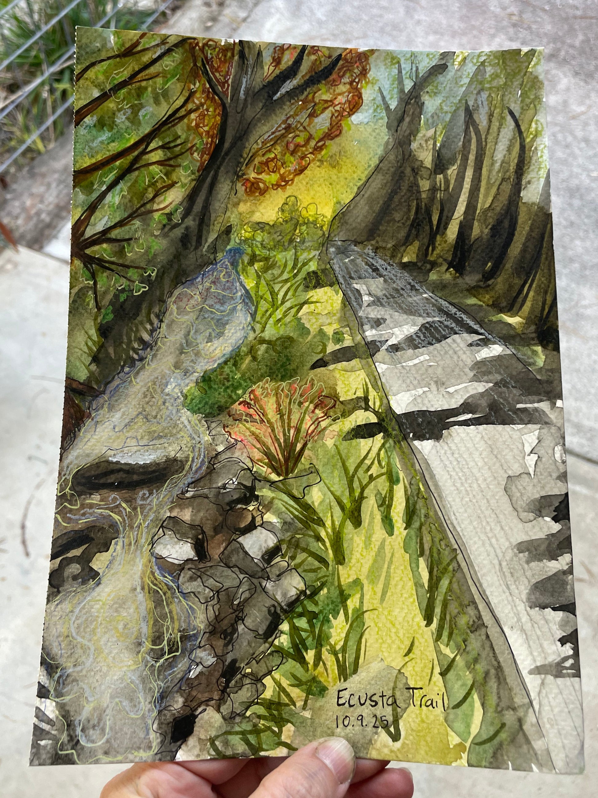 Hand holding a nature-themed painting with trees and leaves on a textured surface.